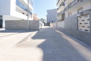 A narrow urban street with modern buildings, a clear sky, and a paved walkway. - GuestHost - Perla Nera Apartment 7 near the sea (Trani)