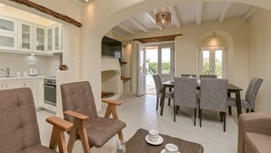 A spacious living area with a dining table, chairs, and a kitchen with white cabinets. - Villa Calivion, Private Outdoor Hot Tub, Furnished Terrace, Shared Pool, Naxos (Naxos)