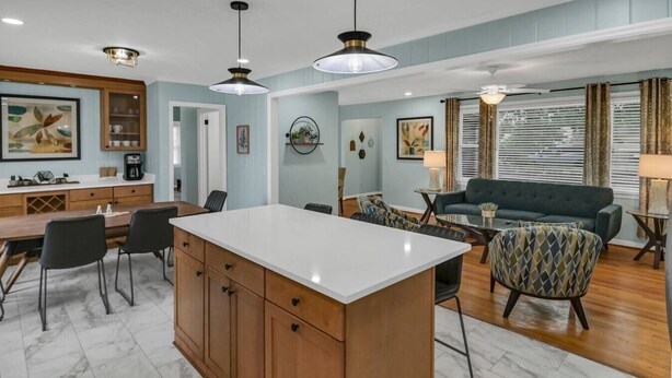 A modern kitchen with a central island, dining area with chairs, a sofa, and a coffee station. - The Garden House | Sleeps 11 | Near USC (Cayce)