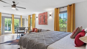 Ein geräumiges Schlafzimmer mit einem großen Bett, einem Deckenventilator, einem Essbereich und Blick durch große Fenster.