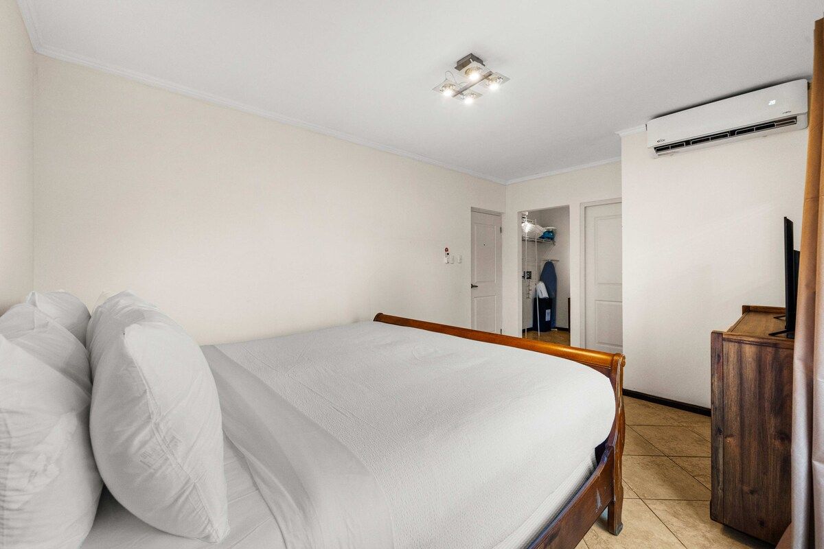 Un dormitorio con cama, cabecero de madera, armario y equipo de aire acondicionado.