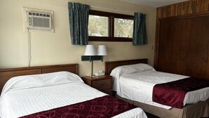 Camera d'albergo con due letti, una finestra con tende, un condizionatore d'aria a parete e un comodino con una lampada.