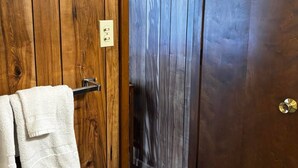 Una porta in legno con un asciugamano appeso a un porta-asciugamani, che dà accesso a una stanza con tappeto viola e pavimento in legno.