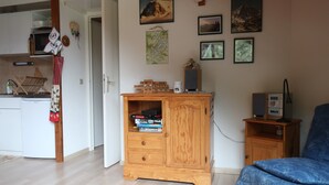 Ein Zimmer mit einem Holzkasten, einem Bett, einem kleinen Tisch und einer Wand mit gerahmten Bildern.