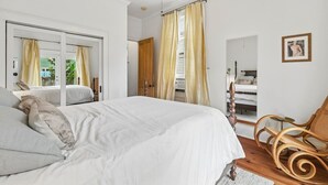 Ein Schlafzimmer mit einem großen Bett, einem Holzstuhl, einem Spiegel und einem Bild an der Wand.