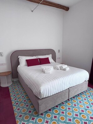 A bed with white bedding and two red pillows, a grey headboard, and a patterned floor. - Relais Totò:vacation home with authentic charm, inspired by  Naples (Campania)