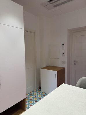 A small, narrow room with white walls, a wooden cabinet, a small refrigerator, and a tiled floor. - Relais Totò:vacation home with authentic charm, inspired by  Naples (Campania)