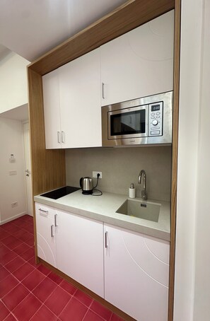 A modern kitchen with white cabinets, a stainless steel microwave, a kettle, and a sink with a faucet. - Relais Totò:vacation home with authentic charm, inspired by  Naples (Campania)