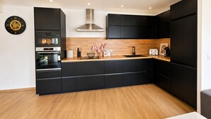 Una cocina moderna con armarios negros, encimera de madera, extractor de acero inoxidable y un reloj en la pared.