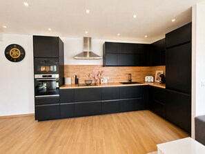 Une cuisine moderne avec des meubles de couleur noire, un plan de travail en bois, une hotte de cuisine en acier inoxydable et une horloge au mur.