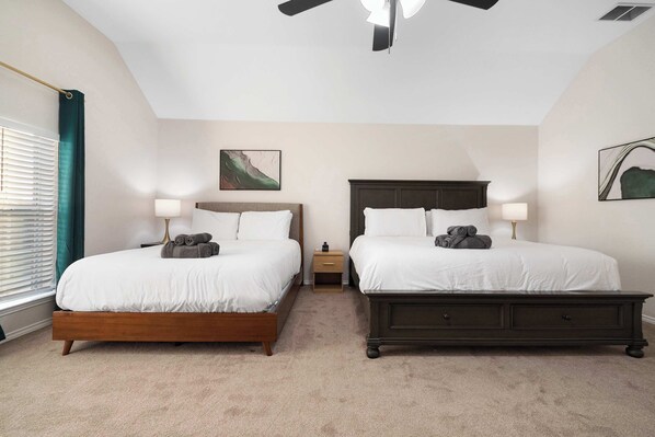 A hotel room with two beds, a ceiling fan, and artwork on the walls.