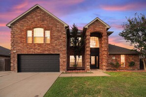 A two-story brick house with a garage, a front porch, and a small front yard.