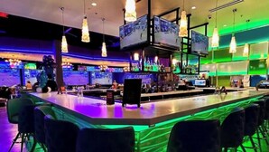 Angolo bar con diversi schermi, luci a sospensione e sgabelli da bar.