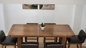 Un tavolo da pranzo rettangolare in legno con sei sedie, una piccola pianta in vaso sul tavolo e due dipinti astratti appesi alla parete soprastante.