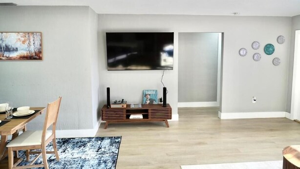 A modern living room with a dining area, a flat-screen TV, and decorative wall art.