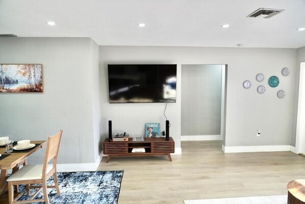 A modern living room with a dining area, a flat-screen TV, and decorative wall art.