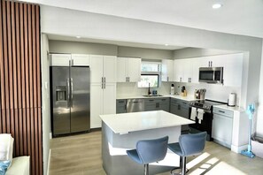 A modern kitchen with stainless steel appliances, a central island with bar stools, and a view of the outdoors. - Family Pool Oasis Near Hard Rock • Beaches • Airport (Hollywood)