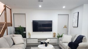 A modern living room with a flat-screen TV, two sofas, a coffee table, and a staircase.
