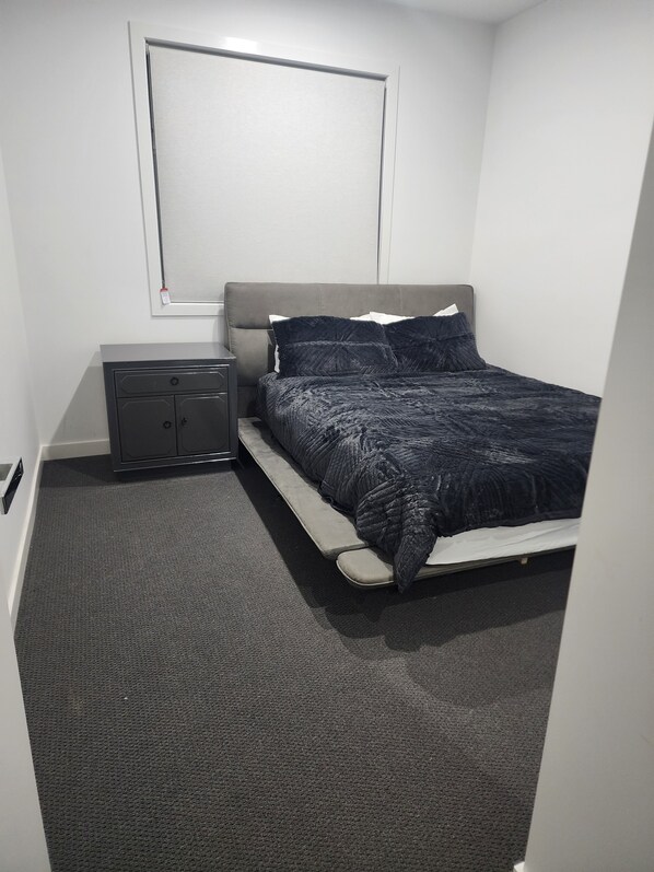 A bedroom with a bed, a nightstand, a dresser, and a wall-mounted shelf.