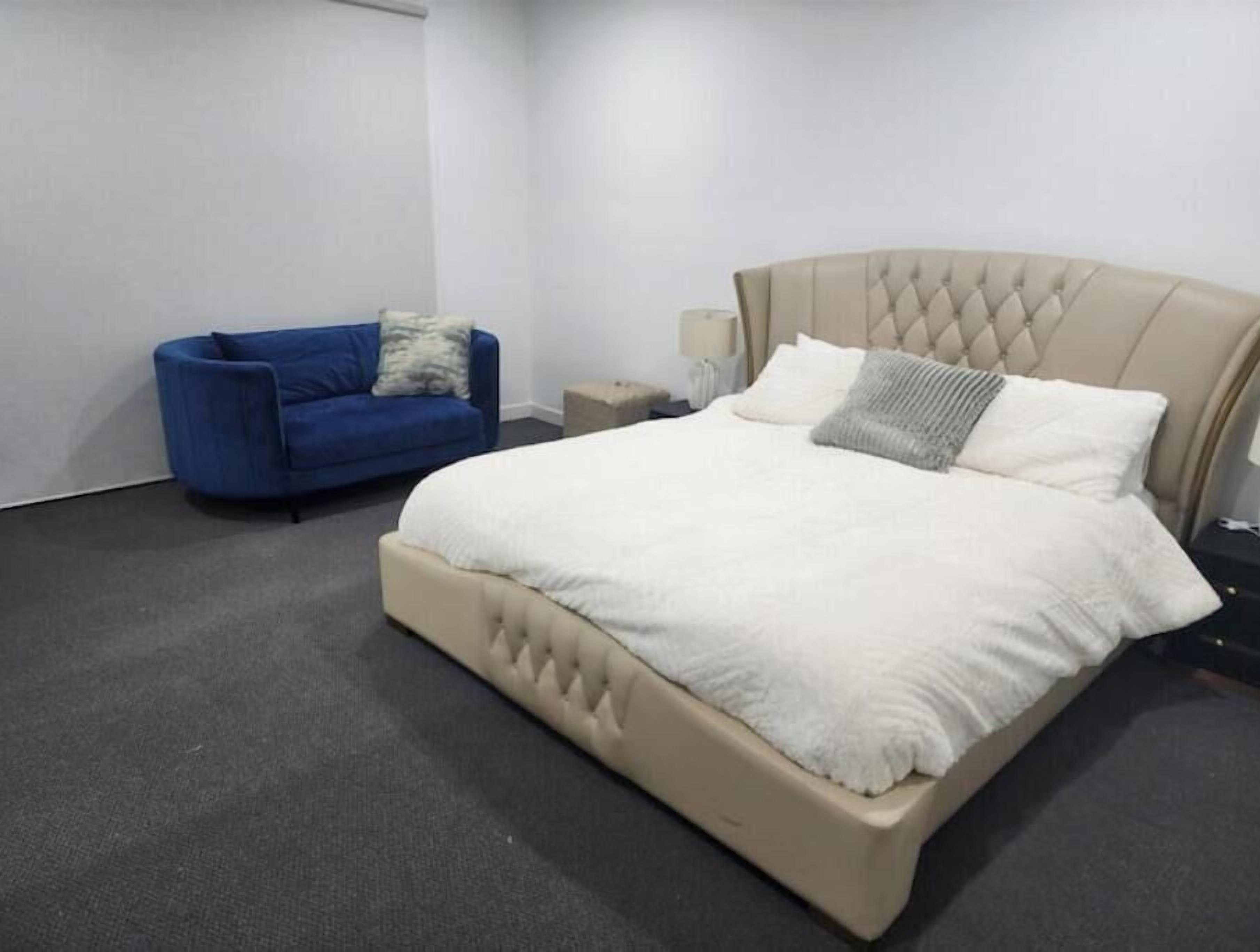 A bedroom with a large bed, a blue sofa, and a nightstand with a lamp.