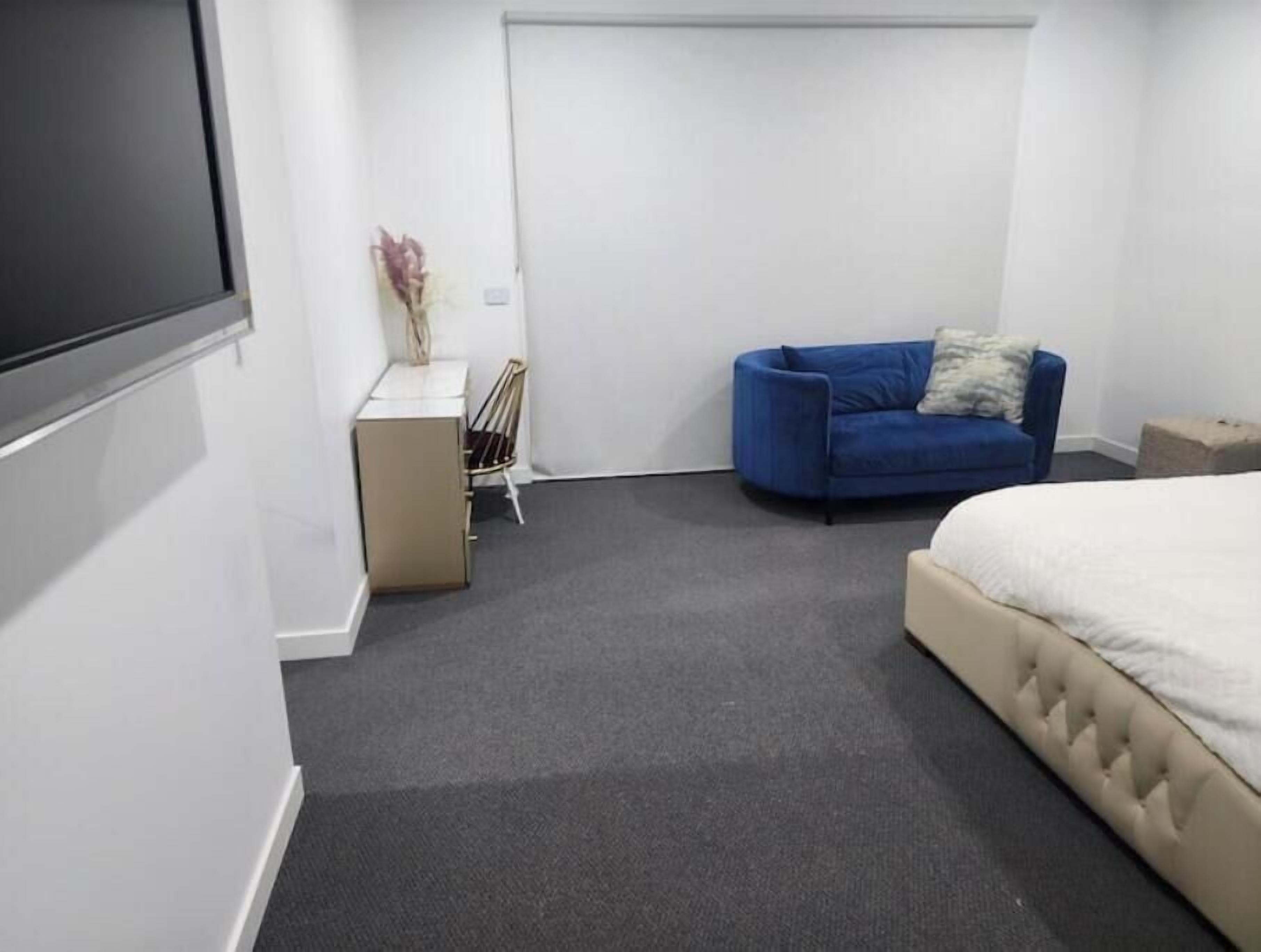 A bedroom with a bed, a blue sofa, a small desk with a chair, and a white door.