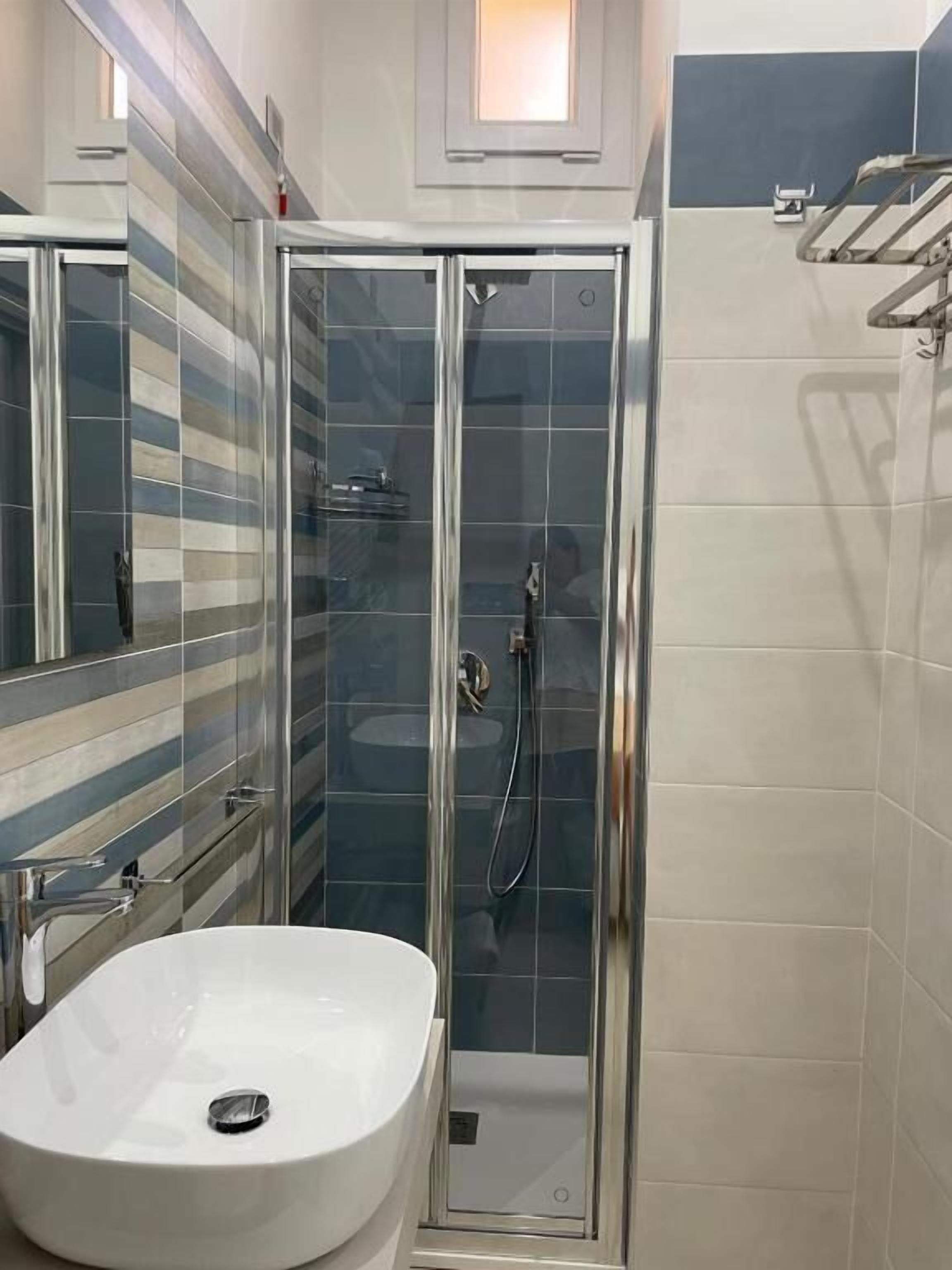 A bathroom with a glass-enclosed shower, a white sink, and a tiled wall with a striped pattern.