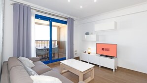 Ein modernes Wohnzimmer mit einer Couch, einem Couchtisch, einem Fernseher und einem Balkon mit Tisch und Stühlen.