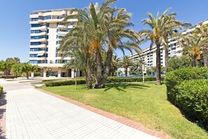 A modern hotel with a central courtyard, palm trees, and a paved walkway. - GuestReady - Beachside apartment with Pool (Alboraya)