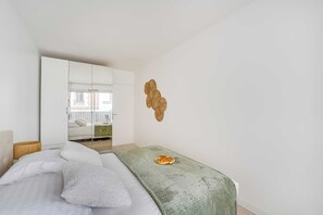 A bedroom with a bed, a green blanket, a wall-mounted decorative piece, and a mirror reflecting a room with a bed and a window. - Spacious Apartment 1br/2p - Auteuil (Paris)