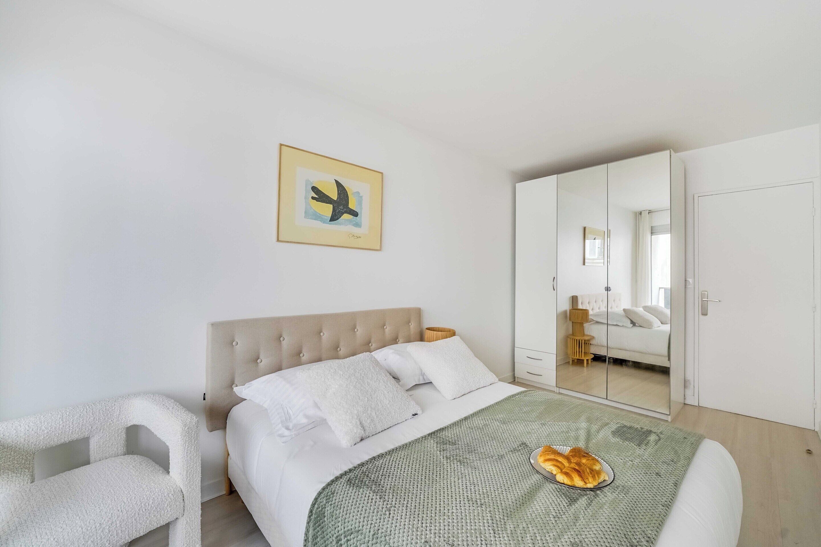 Ein Schlafzimmer mit Bett, Sessel, Spiegel und einem Bild an der Wand.