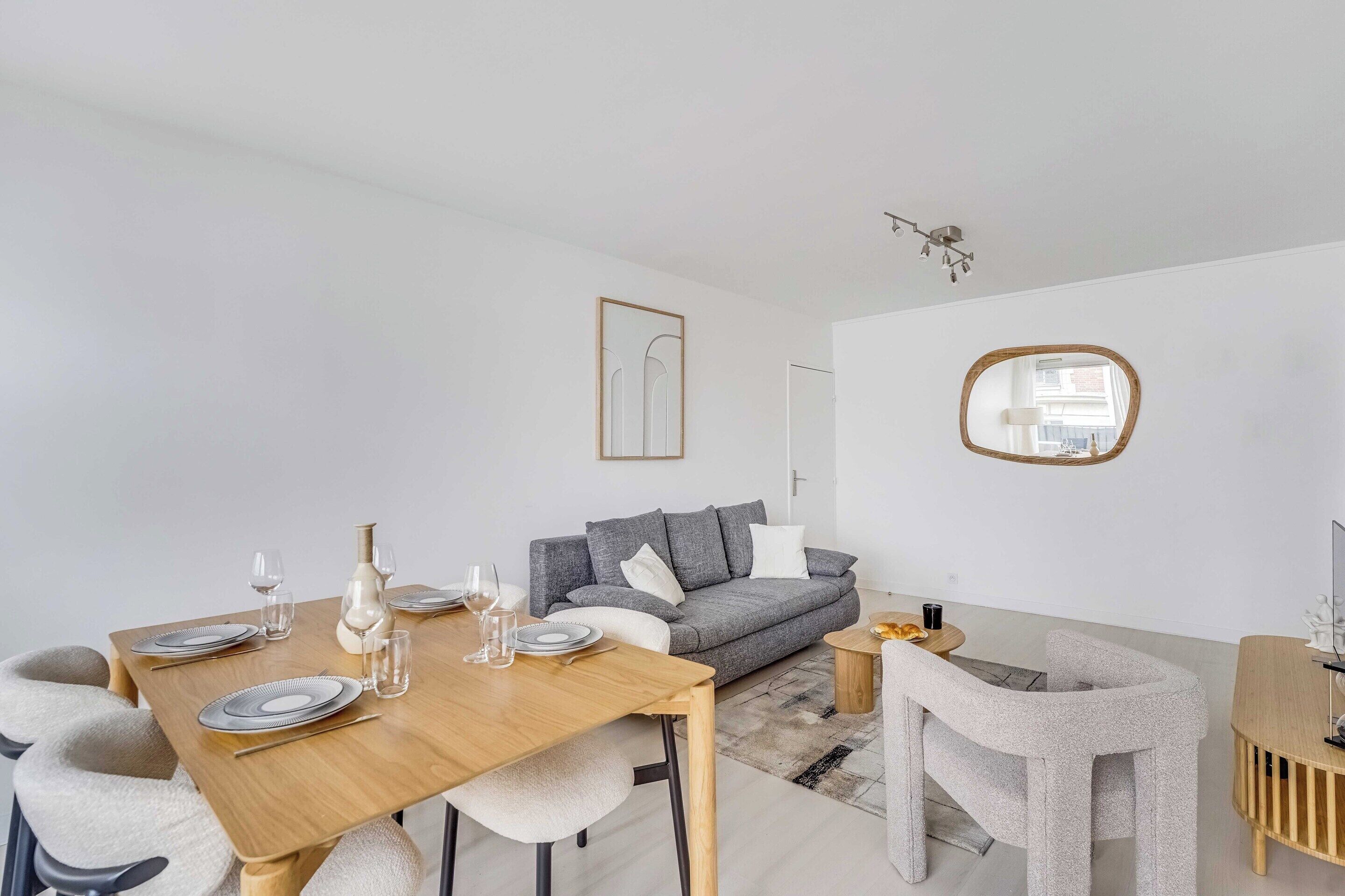A modern living room with a dining area, a grey sofa, a round mirror, and a minimalist decor style.