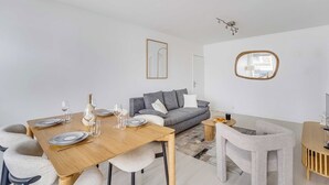 Ett modernt vardagsrum med en matplats, en grå soffa, en rund spegel och en minimalistisk inredningsstil.
