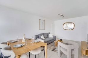 A modern living room with a dining area, a grey sofa, a round mirror, and a minimalist decor style. - Spacious Apartment 1br/2p - Auteuil (Paris)
