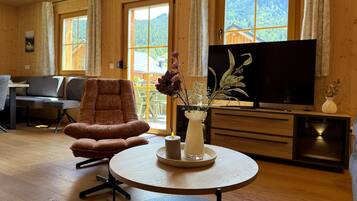Ein Holzinnenraum mit einer Couch, einem runden Tisch mit Kerze, einem Fernseher und einem Fenster mit Blick auf Grünflächen.