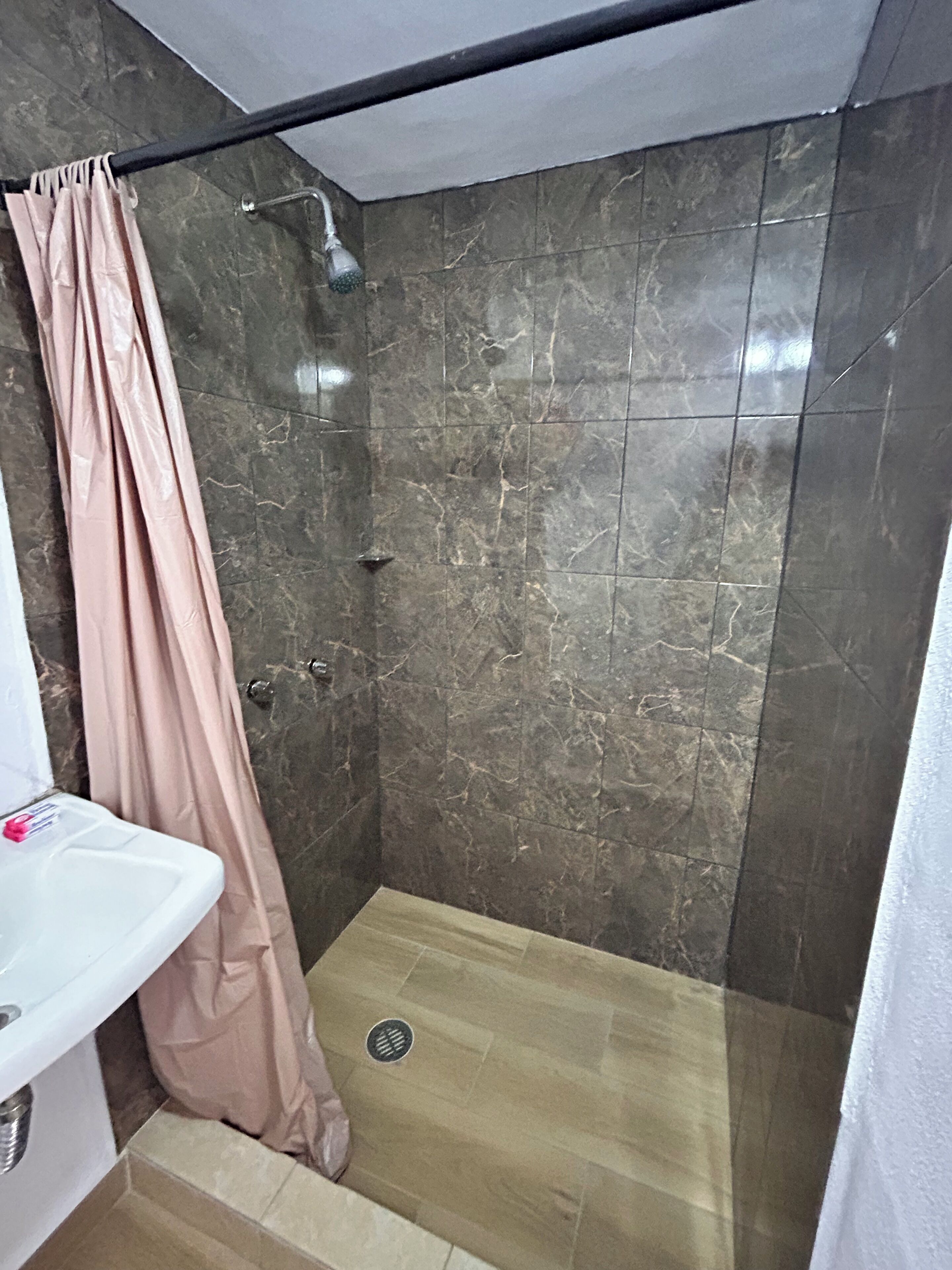 Un baño con ducha, lavabo y piso de baldosas.