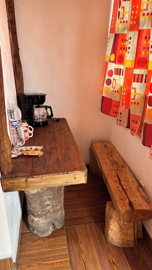 A rustic wooden table with a coffee maker, a water bottle, and a snack package. A bench is against the wall, and a colorful quilt hangs above. - Hospedaje La Joya By GEstores (Mineral del Chico)