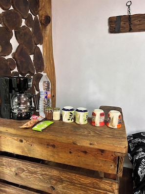 Ein Holztisch mit einer Kaffeemaschine, einer Wasserflasche, Gläsern und Tassen.