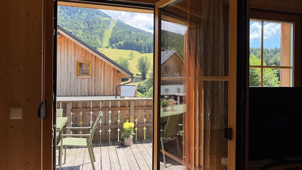A wooden cabin with a sliding glass door leading to an outdoor deck with a table and chairs. - Hideaway Chalets Loser - 5 (Altaussee)