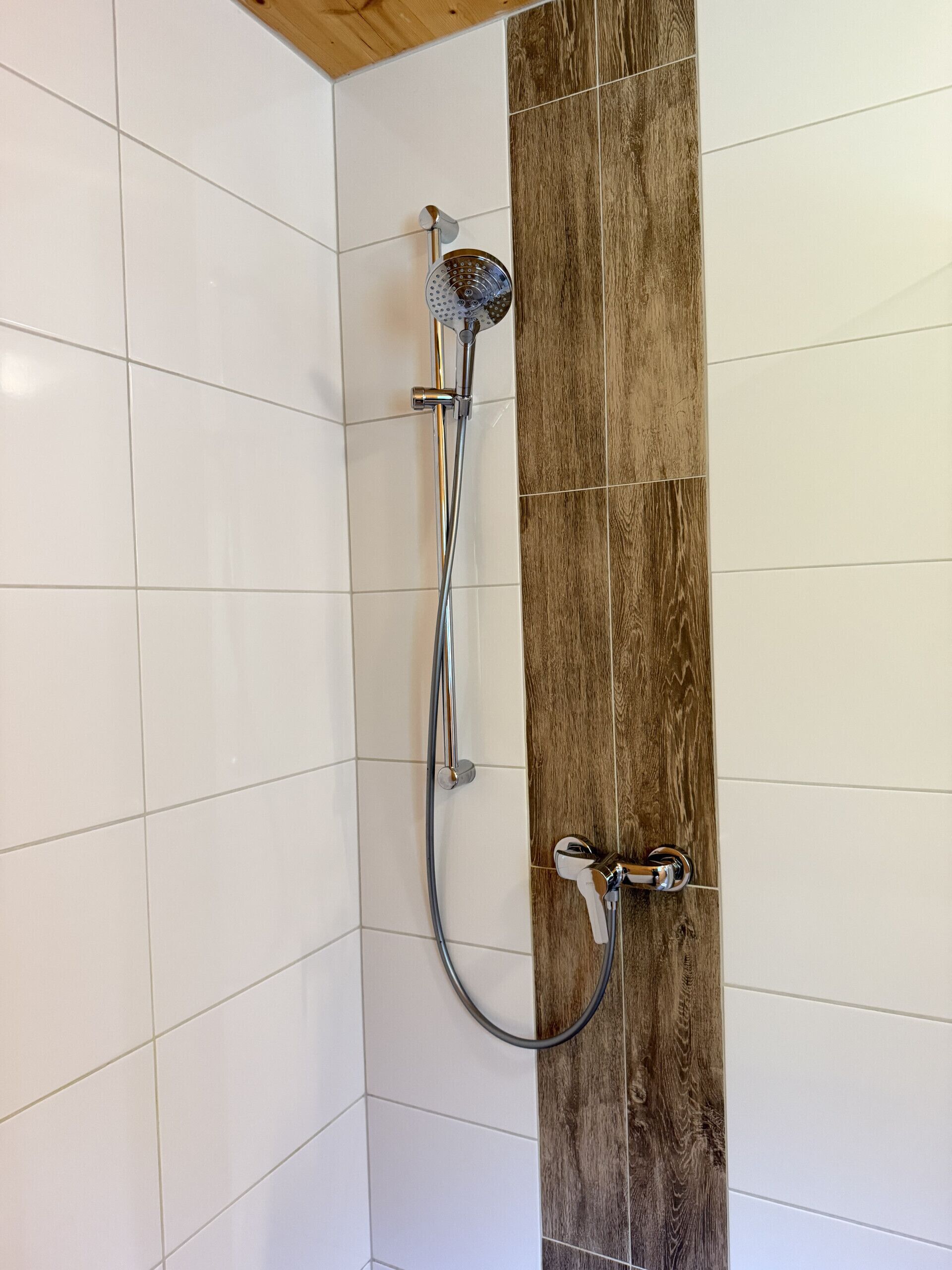 Eine Dusche mit Holzwandverkleidung, weißen Fliesen und einem chromfarbenen Duschkopf und Brauseschlauch.