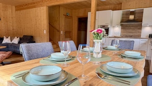 A wooden interior with a dining table set for four, a sofa, and a kitchen area. - Hideaway Chalets Loser - 5 (Altaussee)