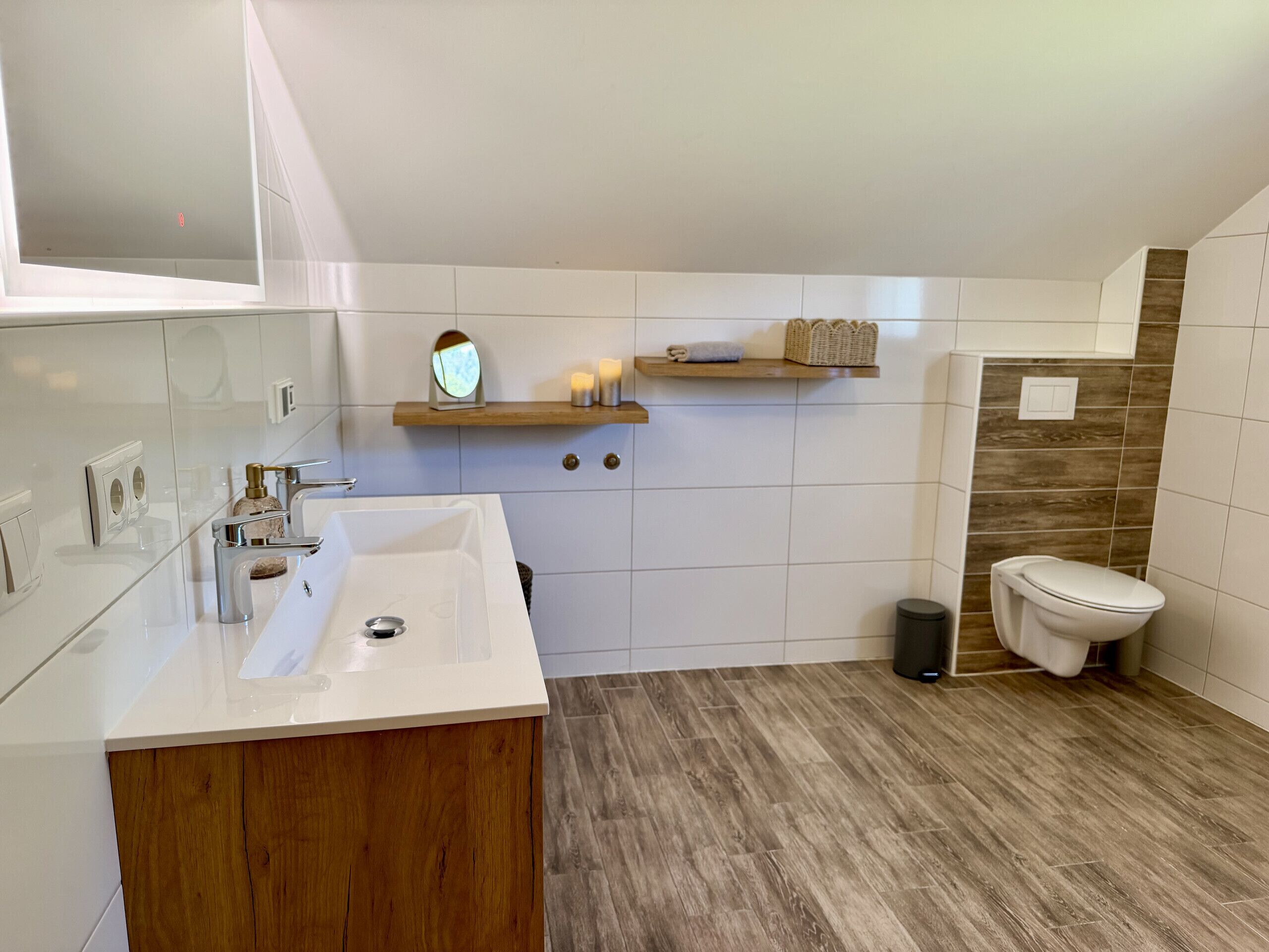 Ein Badezimmer mit einem Holzbadezimmer-Möbel, einem Spiegel, einem Waschbecken, einer Toilette und einem Regal mit Kerzen und einer Uhr.