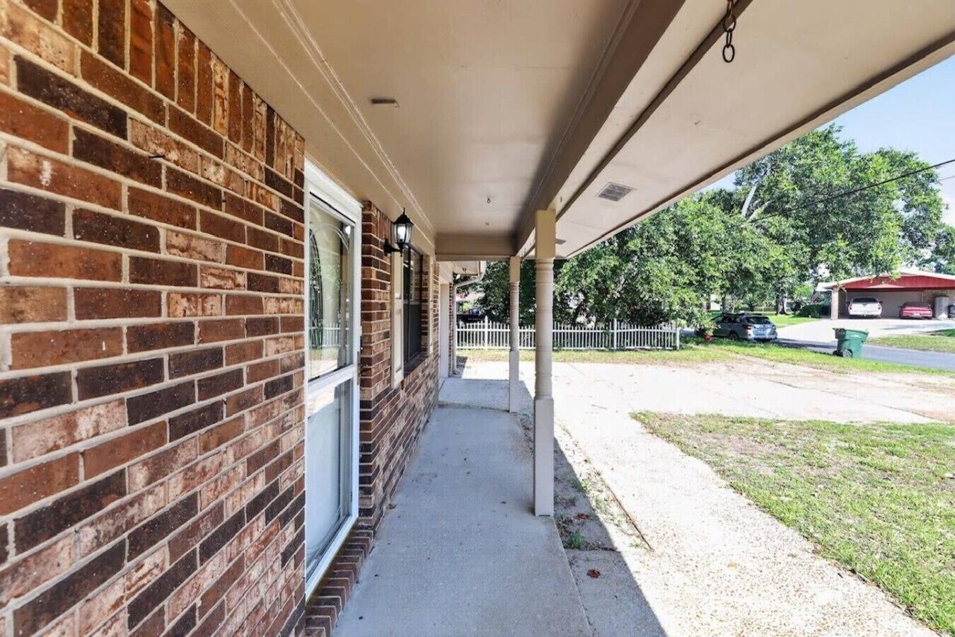 A covered porch with a brick exterior, a clear view of the street, and a fenced yard.