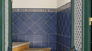 Una escalera con paredes de azulejos azules y puertas verdes, que conduce a una habitación con un cuadro en la pared.
