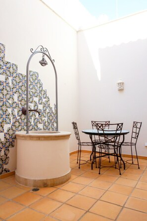 Une terrasse avec une table ronde et des chaises, une fontaine décorative et des carreaux à motifs sur le mur.