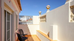 Un balcón con una silla, una pared blanca y una barandilla de metal.