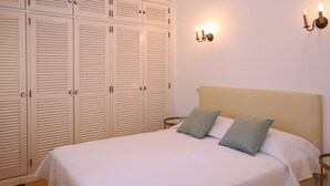 Un dormitorio con cama, dos almohadas, una mesita de noche, una lámpara de pared y un armario con puertas batientes.