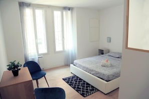 Ein Schlafzimmer mit Bett, Schreibtisch, Stuhl und einem Fenster mit Vorhängen.