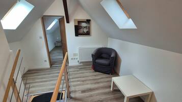 Ein Schlafzimmer im Loft-Stil mit schrägen Wänden, Dachfenstern, einer Heizung, einem schwarzen Stuhl und einem kleinen Tisch.
