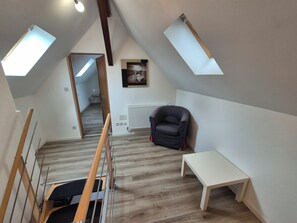 Ein Schlafzimmer im Loft-Stil mit schrägen Wänden, Dachfenstern, einer Heizung, einem schwarzen Stuhl und einem kleinen Tisch.