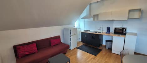 Un espacio habitable compacto con kitchenette, un sofá, una mesita y una zona de comedor.